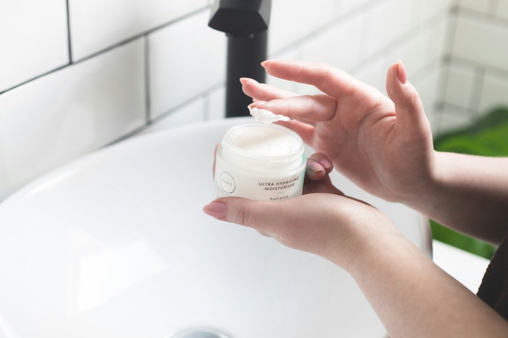 Person dispensing face cream onto fingers at a bathroom sink.